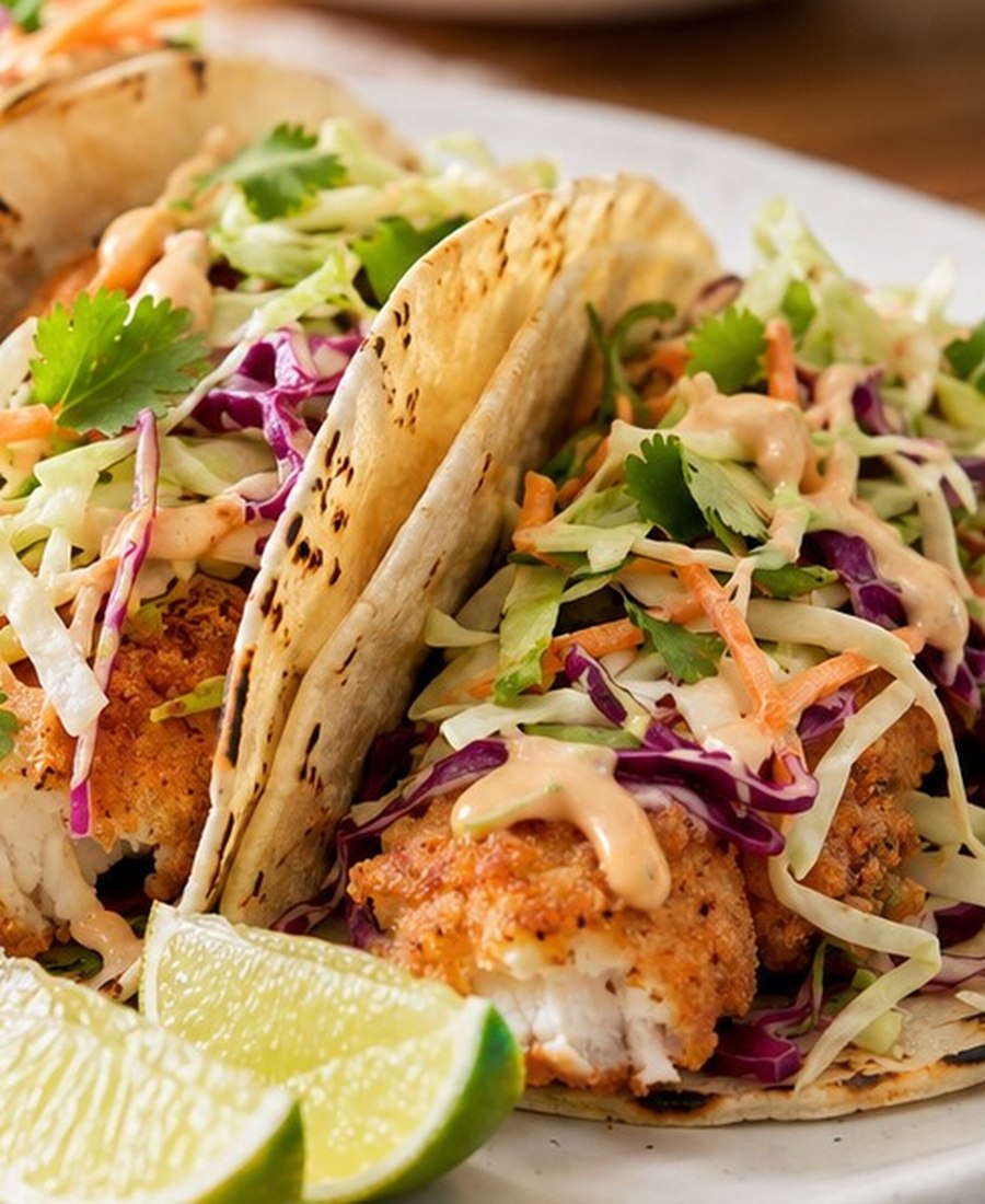 Crispy fish tacos with colourful slaw, lime wedges and creamy sauce