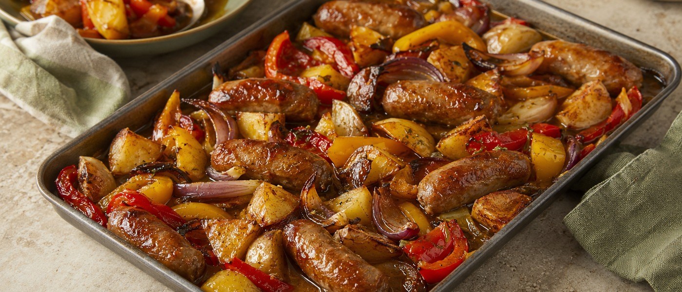 Roasted sausages, potatoes, peppers and red onions in a large tray